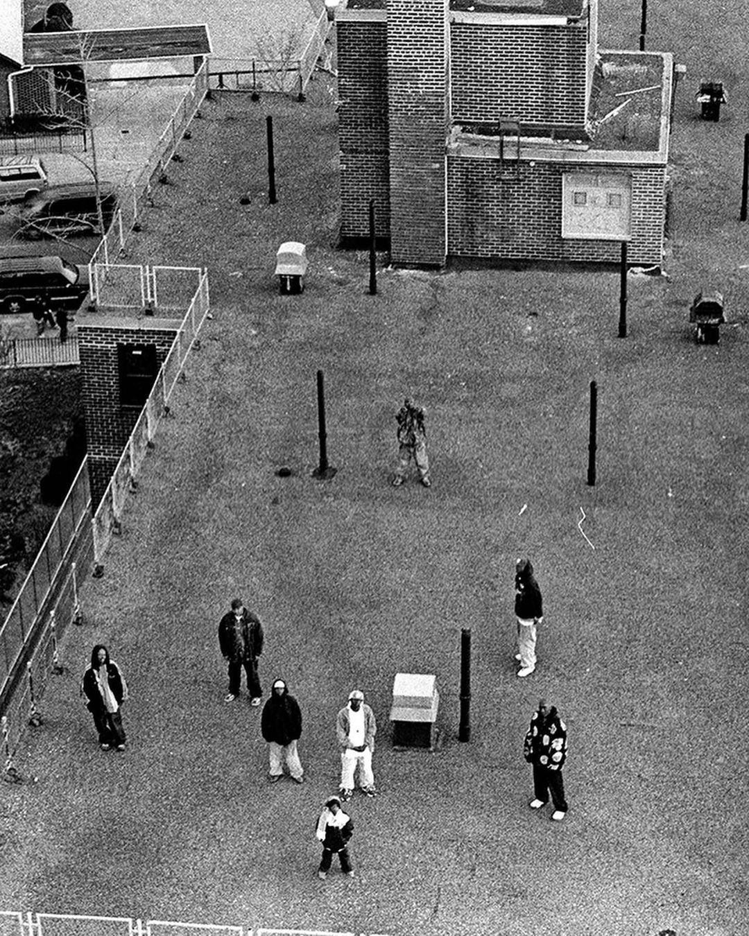 High-angle monochrome aerial view of several people gathered in a paved courtyard by a brick building in New York by Boogie.