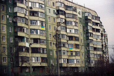 A massive multi-story residential apartment building exterior with weathered pale green facade and numerous balconies.