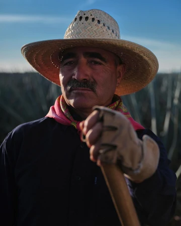 Portrait of a weathered farmer in a straw hat with field in background. Authentic farm lifestyle image, outdoor worker with hand tools.