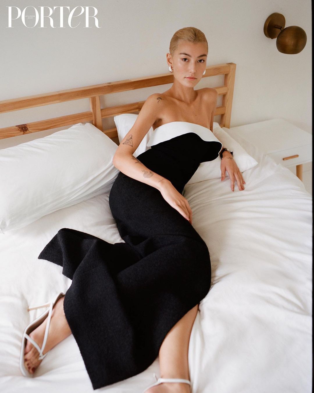 Elegant woman in a black and white dress poses on a bed in a light-filled room, embodying fashion and interior style.