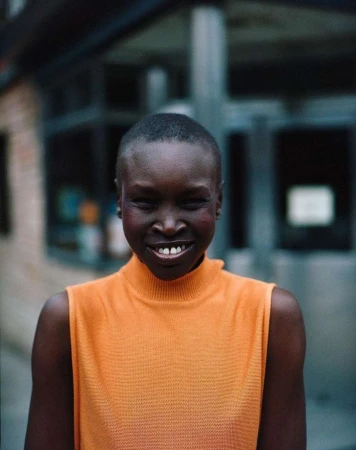 Portrait of a smiling adult woman with short hair wearing an orange top, with blurred urban background.