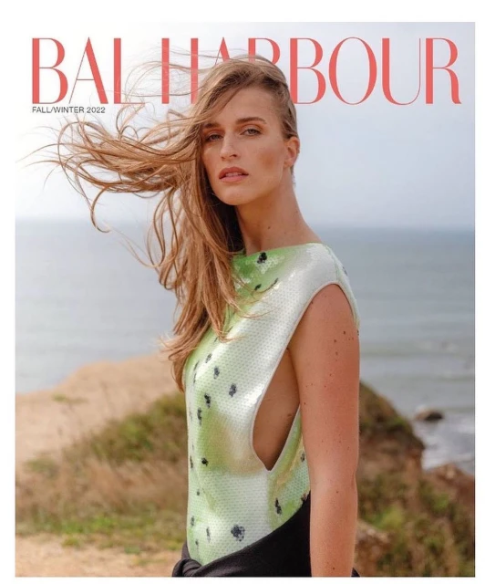 Magazine cover featuring a blonde woman with wind-blown hair, wearing a sleeveless dress, standing on a cliffside with ocean backdrop.