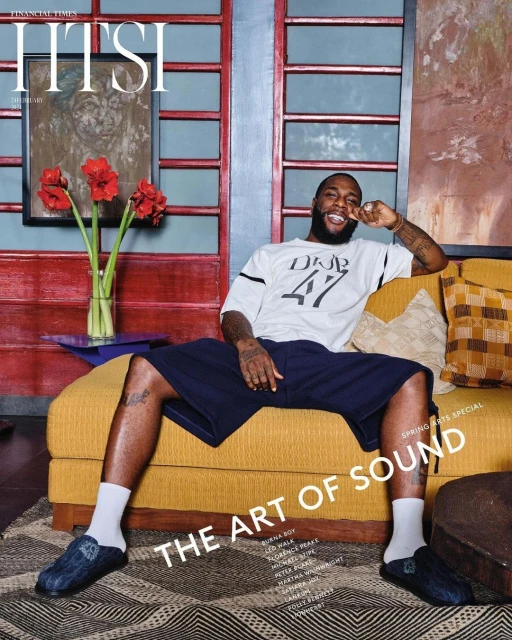 Magazine cover featuring a Black adult male reclining on a yellow couch in a relaxed pose, wearing casual clothing, set in an indoor environment.