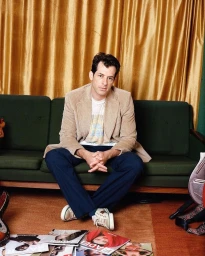 Mark Ronson seated cross-legged on a green velvet sofa wearing a tan corduroy blazer and blue trousers, photographed by Brad Ogbonna.