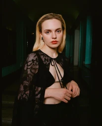 Portrait of a blonde woman wearing a black lace capelet and holding hands in a dimly lit hallway.