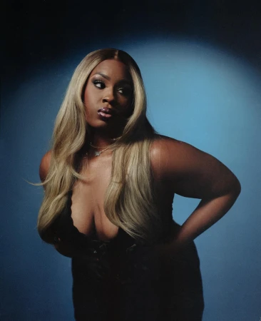 Portrait of a black woman with long blonde hair wearing a black top against a dramatic blue spotlight background.