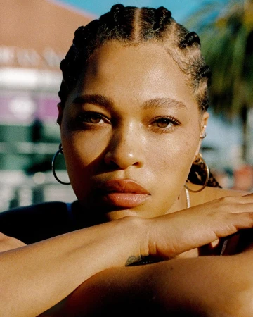 Close-up portrait of a woman with braided hair and hoop earrings resting her chin on her crossed arms outdoors in Los Angeles.