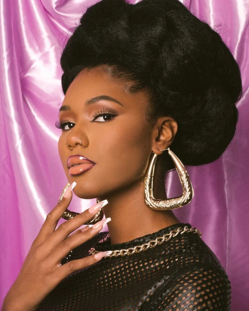 Portrait of a woman with large afro hairstyle wearing earrings and a mesh top with a pink satin background in a photo studio.