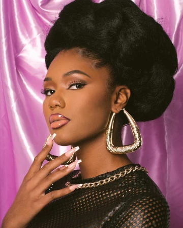 Portrait of a woman with large afro hairstyle wearing earrings and a mesh top with a pink satin background in a photo studio.