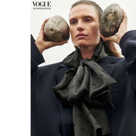 Model holding two large stones up to her head while wearing a dark jacket and satin scarf by Branislav Simoncik