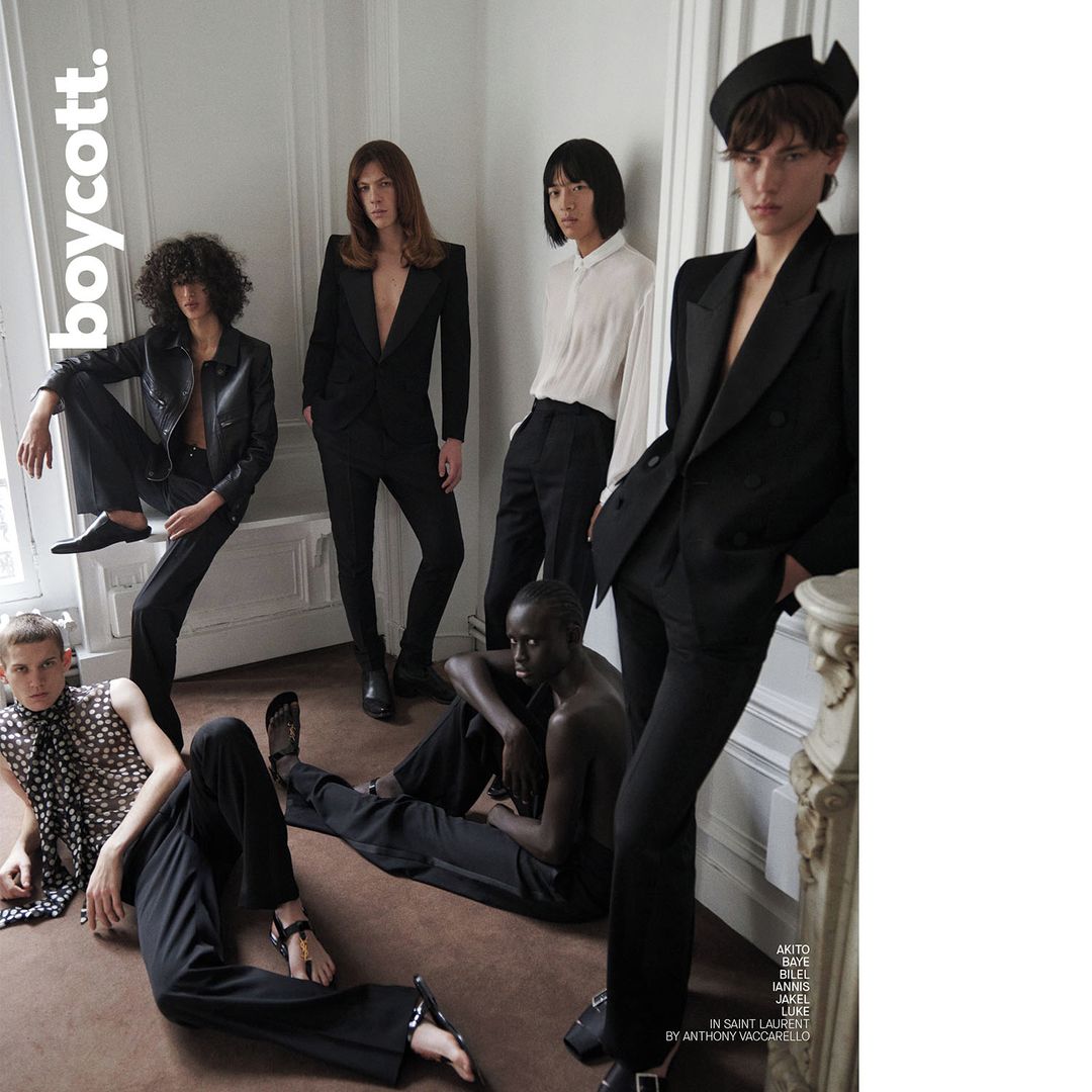 Editorial fashion shot of six models in a photo studio wearing black and white clothing, striking poses against a plain white wall.