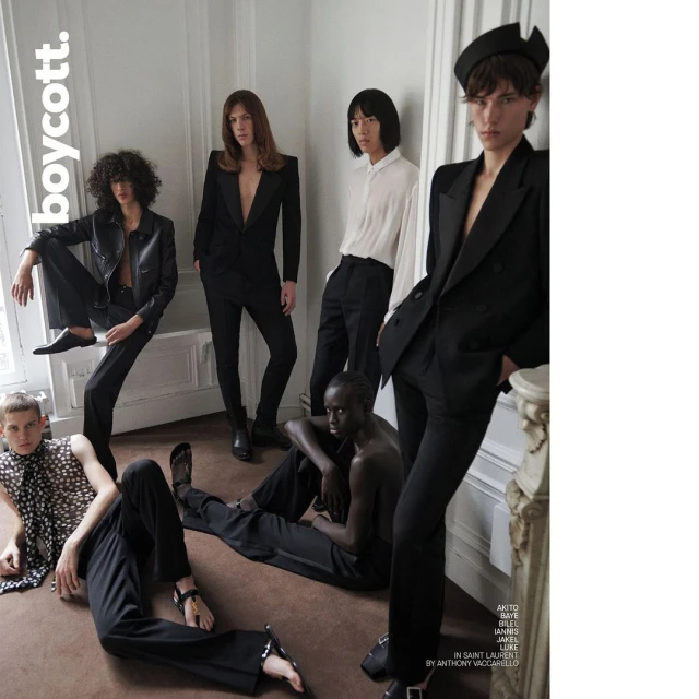Editorial fashion shot of six models in a photo studio wearing black and white clothing, striking poses against a plain white wall.