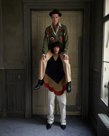 Two male models posing indoors with one carrying the other on his shoulders in a styled editorial fashion photograph