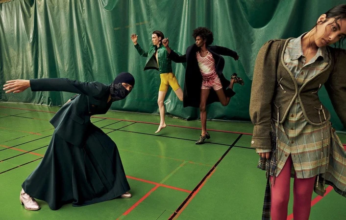 Editorial fashion image of four models in a gymnasium with various poses and apparel, including a balaclava, jacket, skirt, and shorts.