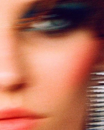 Close-up portrait of a woman with motion blur, vibrant blue eyeshadow, and pink lipstick photographed by Branislav Simoncik in Paris.