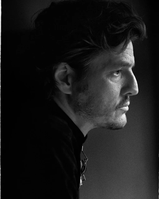 Black and white portrait of an adult male with dark hair in profile, wearing a dark turtleneck shirt, set against a dark background.