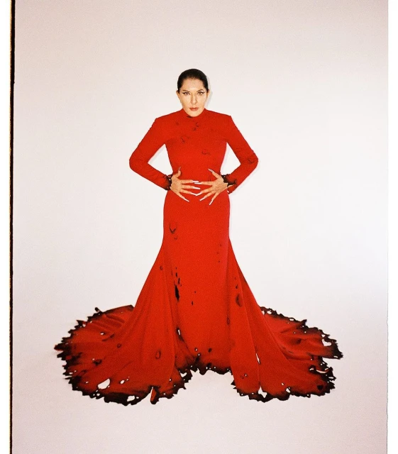 Adult woman in a full-length red gown with a black lace hem poses in a photo studio with hands on her stomach, creating a strong fashion moment.