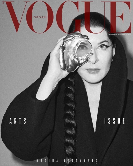 Vogue Portugal magazine cover featuring a woman wearing a black coat with sculptural hand jewelry over one eye, against a gray background.