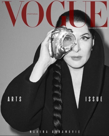 Vogue Portugal magazine cover featuring a woman wearing a black coat with sculptural hand jewelry over one eye, against a gray background.