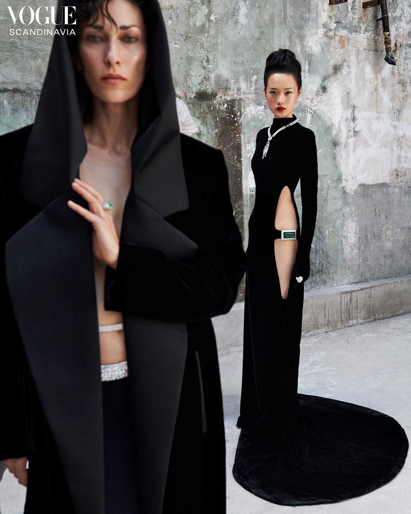 Two women in elegant black dresses and jewelry pose against a textured wall in a fashion editorial for Vogue Scandinavia, full shot.