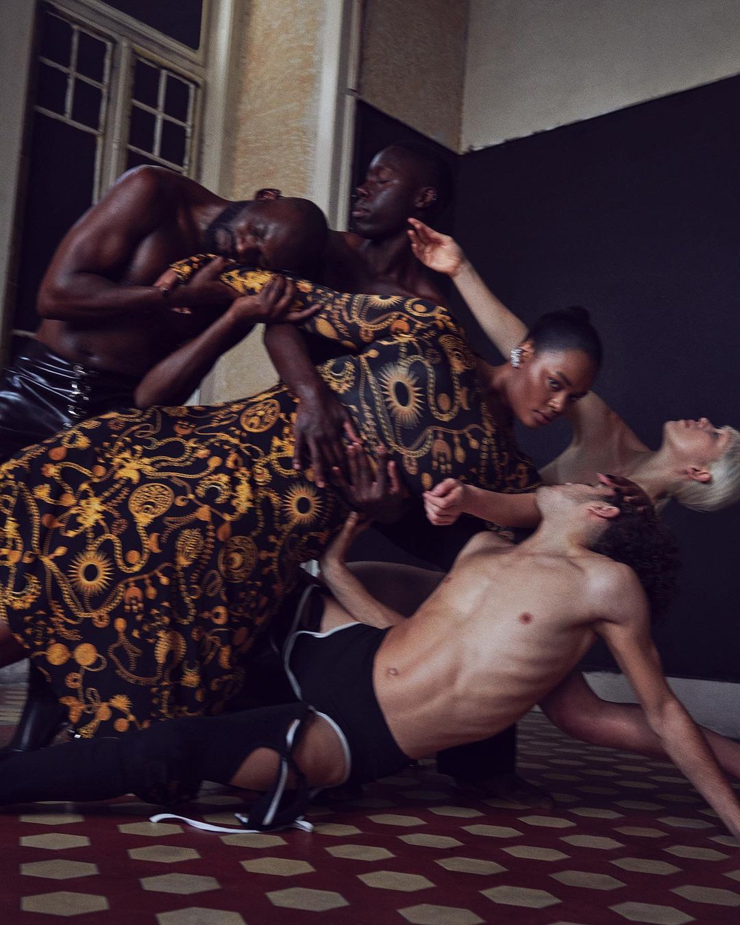 Editorial fashion shot of diverse models interacting in an indoor location, featuring bold colors, patterned fabric, and unique poses.