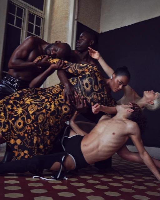Editorial fashion shot of diverse models interacting in an indoor location, featuring bold colors, patterned fabric, and unique poses.