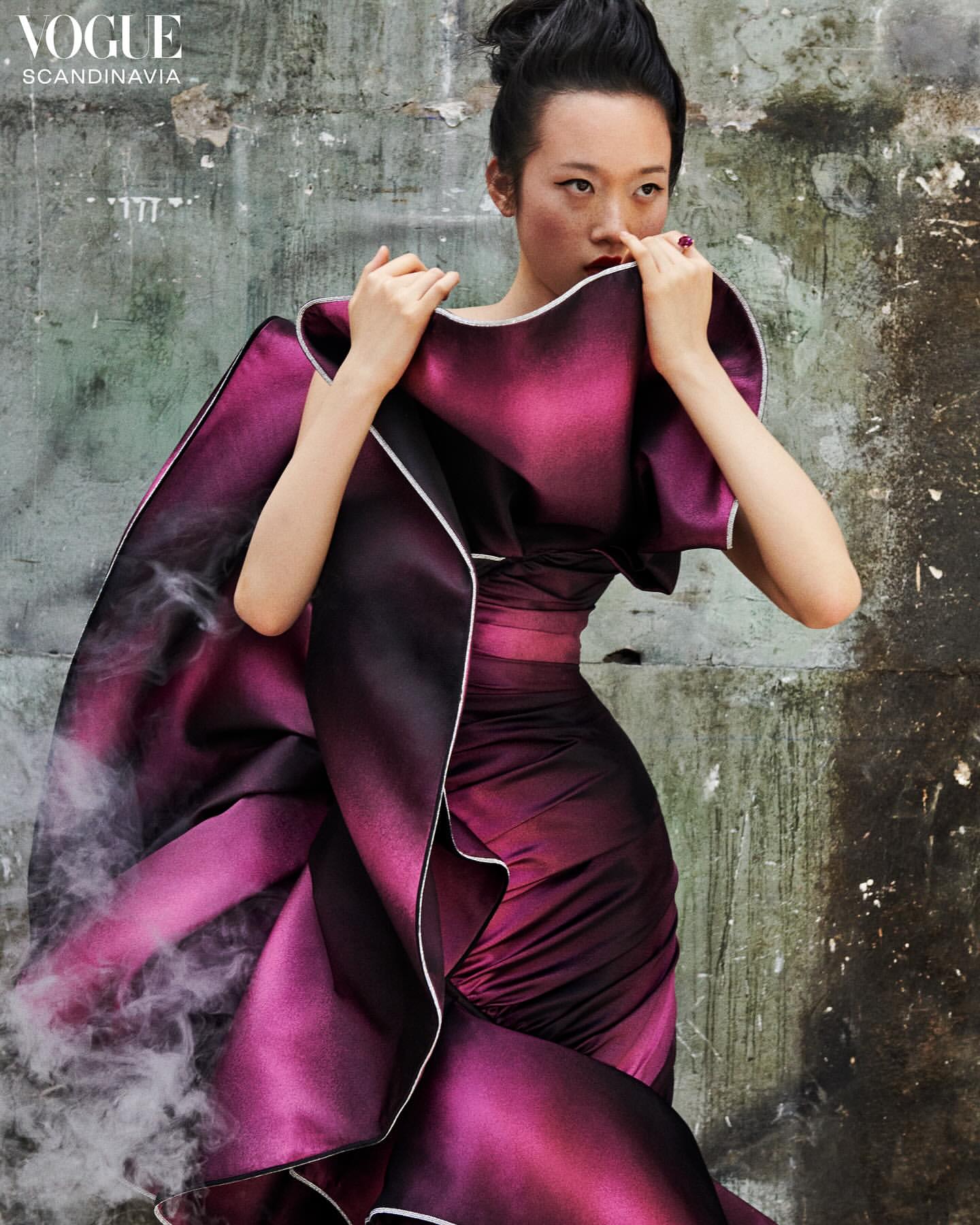 Fashion editorial shot: Asian woman in a magenta gown poses against a textured wall with artificial smoke adding an atmospheric touch.