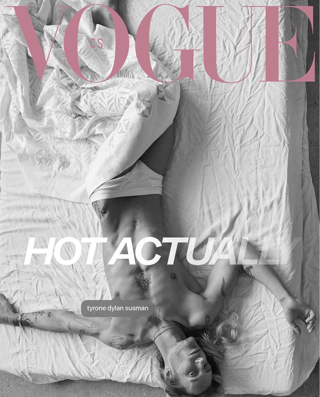 Shirtless man, Tyrone Dylan Susman, poses on a white bed with tattoos visible, featured in Vogue magazine cover with pink logo.
