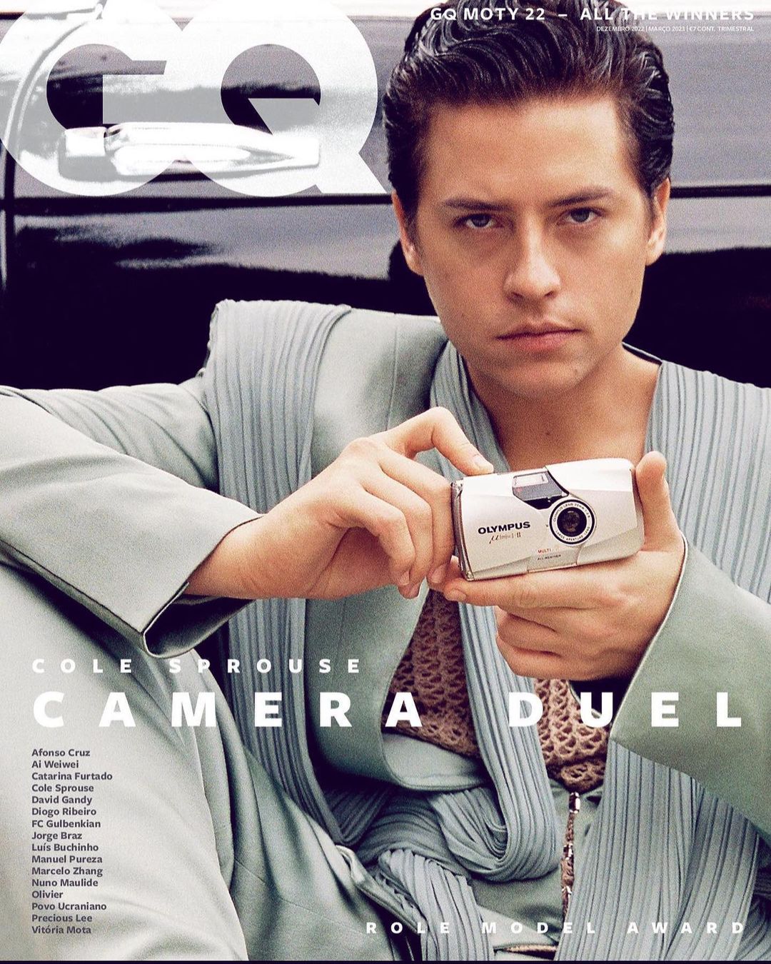 Magazine cover featuring Cole Sprouse holding a vintage Olympus camera, wearing a light-green suit with GQ magazine logo at the top.