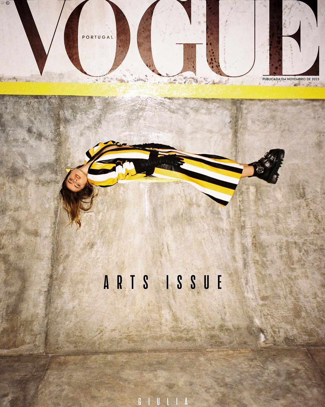 Vogue Portugal magazine cover featuring a woman in a yellow and black striped dress, lying on a concrete surface, with 'Arts Issue' text.
