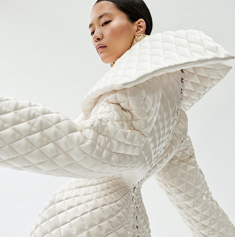 Asian woman poses in an off-white quilted dress with a large collar against a clean white background in a studio fashion shot.