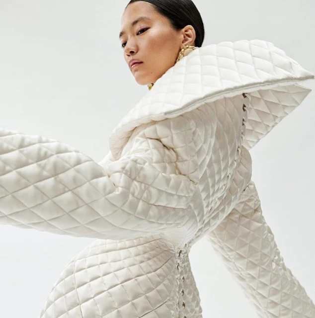 Asian woman poses in an off-white quilted dress with a large collar against a clean white background in a studio fashion shot.