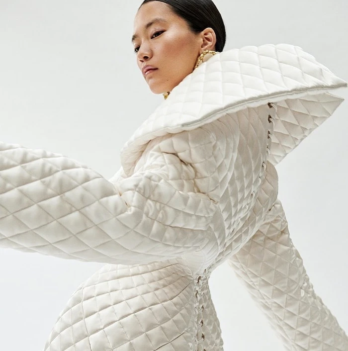 Model wearing a white quilted coat with a dramatic oversized collar against a plain white background