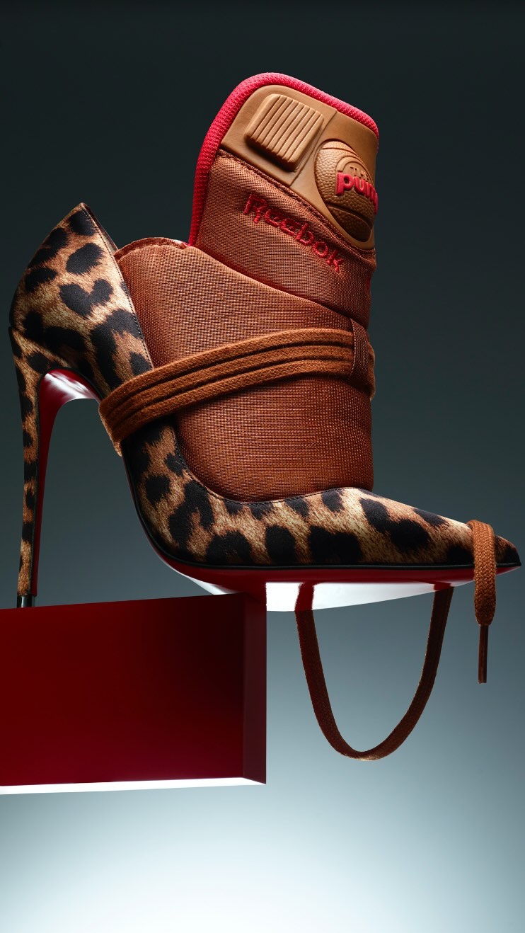 Hybrid shoe art featuring a Reebok sneaker combined with a leopard-print high heel, creatively displayed on a red platform against a grey background.
