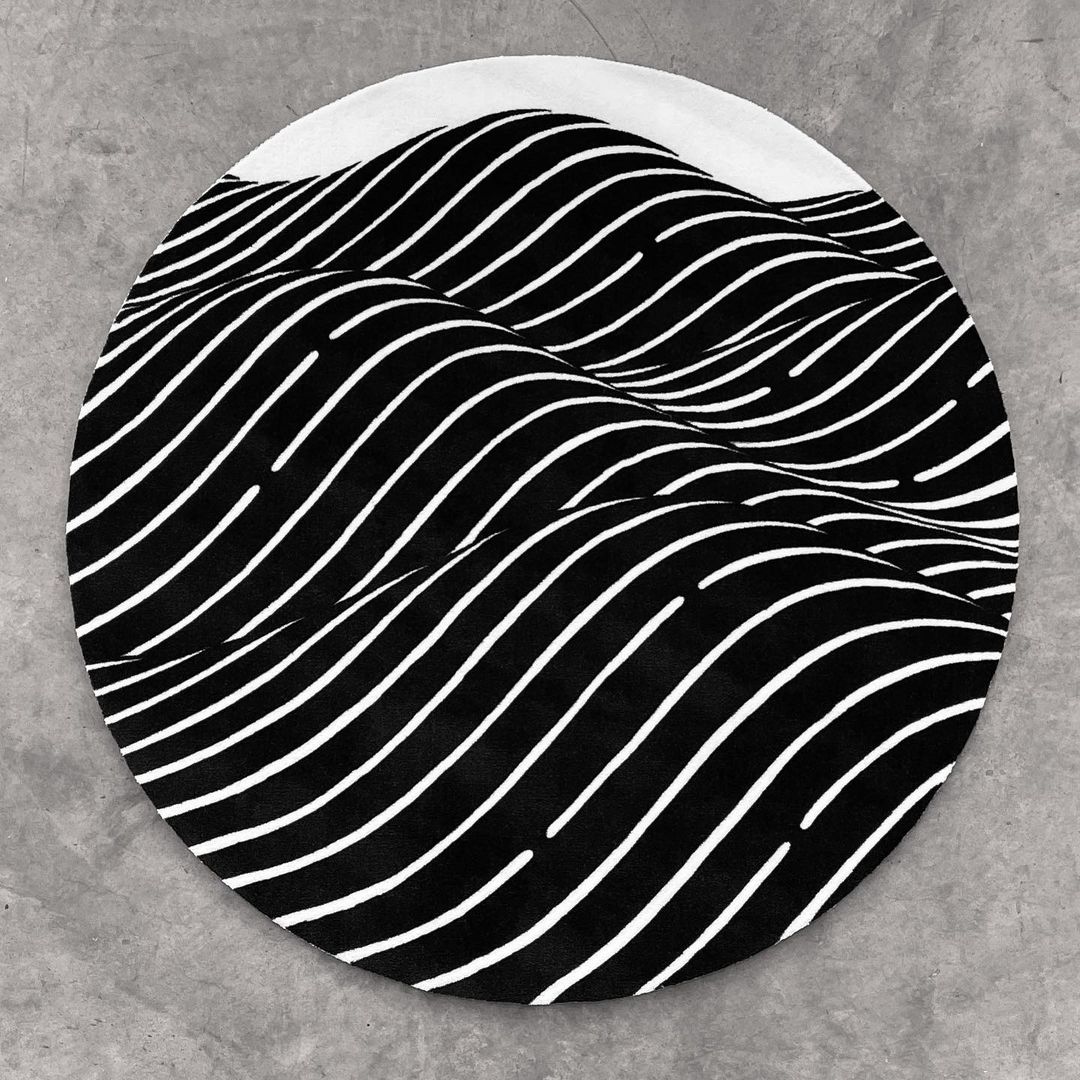 Abstract rug with a wave pattern of black and white stripes forming a circular shape on a light grey concrete background.