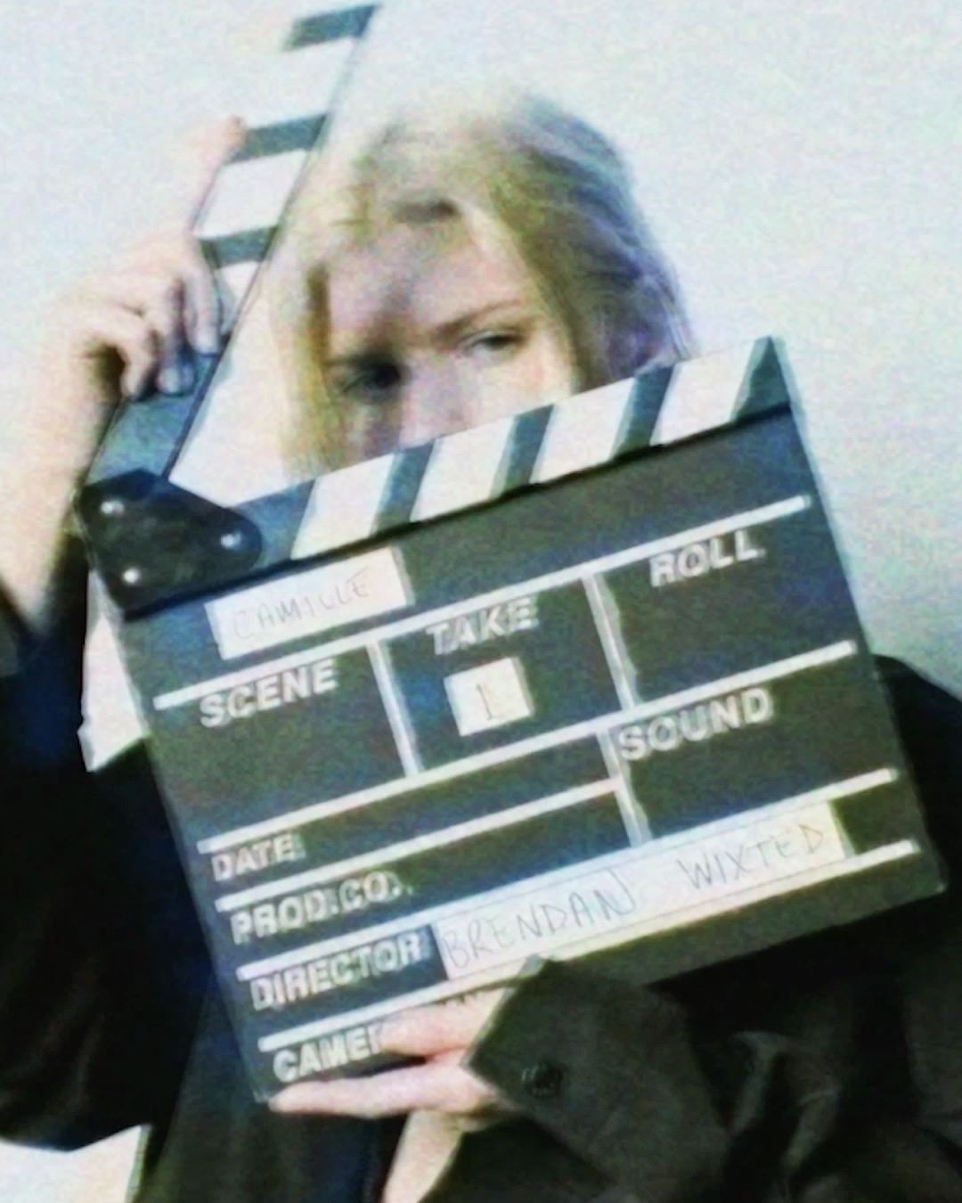 Person holding a film slate with title and production information. Black and white clapperboard and blonde hair woman.