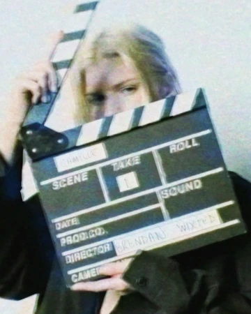 Person holding a film slate with title and production information. Black and white clapperboard and blonde hair woman.