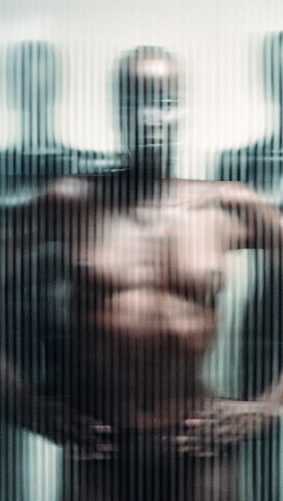Distorted view of a group of figures in front of a vertically striped background, using blurred focus and strong contrasts.