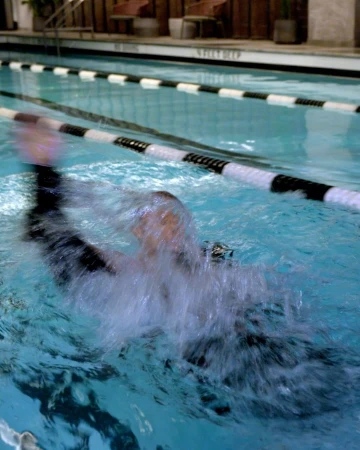 Person swimming in an indoor pool with clear blue water, black and white lane dividers, and shallow depth marker.