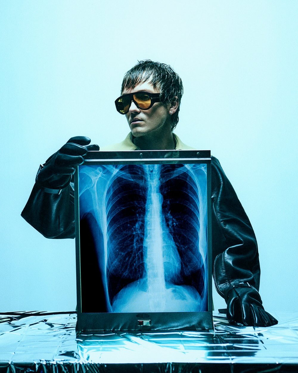 Adult holding chest x-ray in modern medical scene. Stylish eyeglasses and gloves add a contemporary fashion aesthetic.