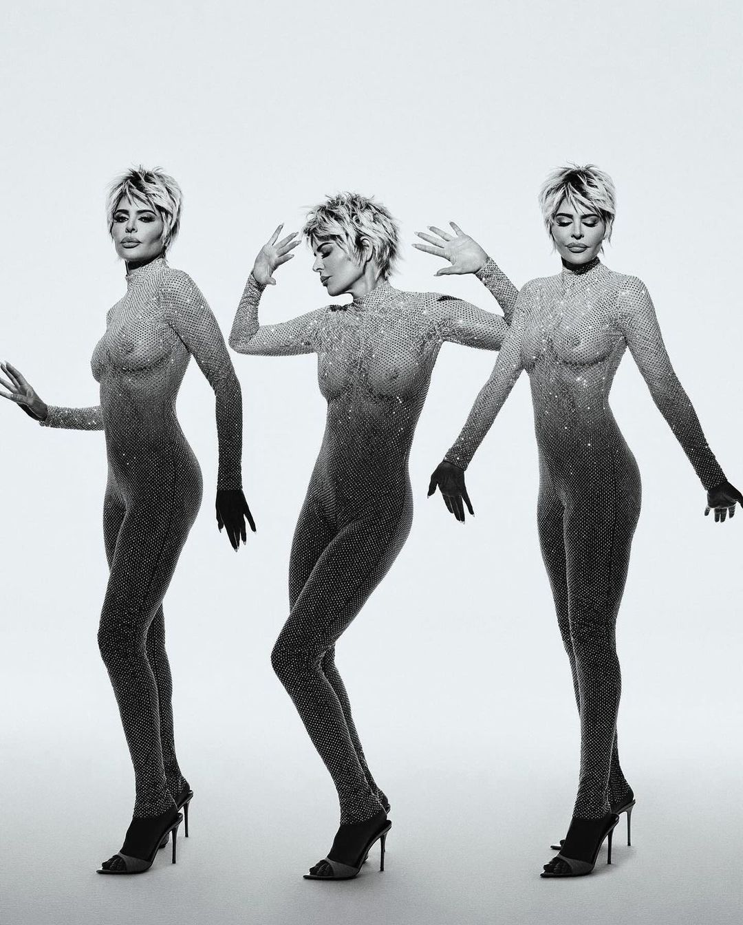 Three adult women posing in sheer catsuits and high heels on a white background, showcasing a mirrored, monochromatic fashion shot.