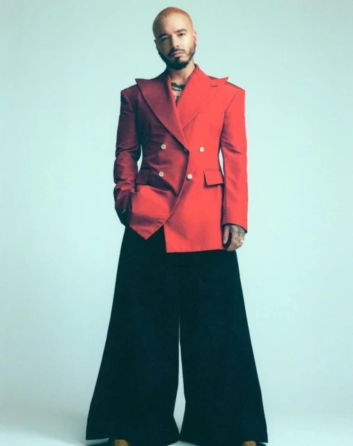 Full-length shot of male fashion model in a red double-breasted blazer and black wide-leg pants posing on a light blue background.