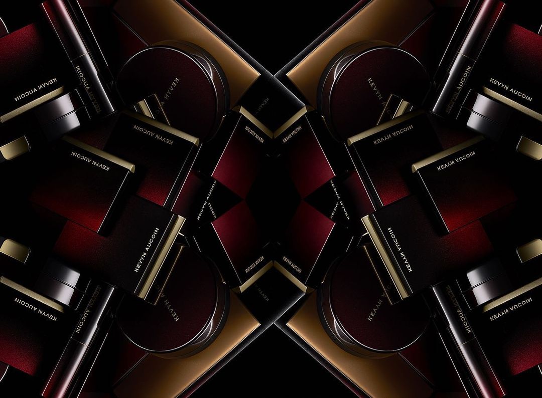 Elevated shot of an array of Kevyn Aucoin makeup products including mascara, pressed powder, and contour palettes on a dark surface.