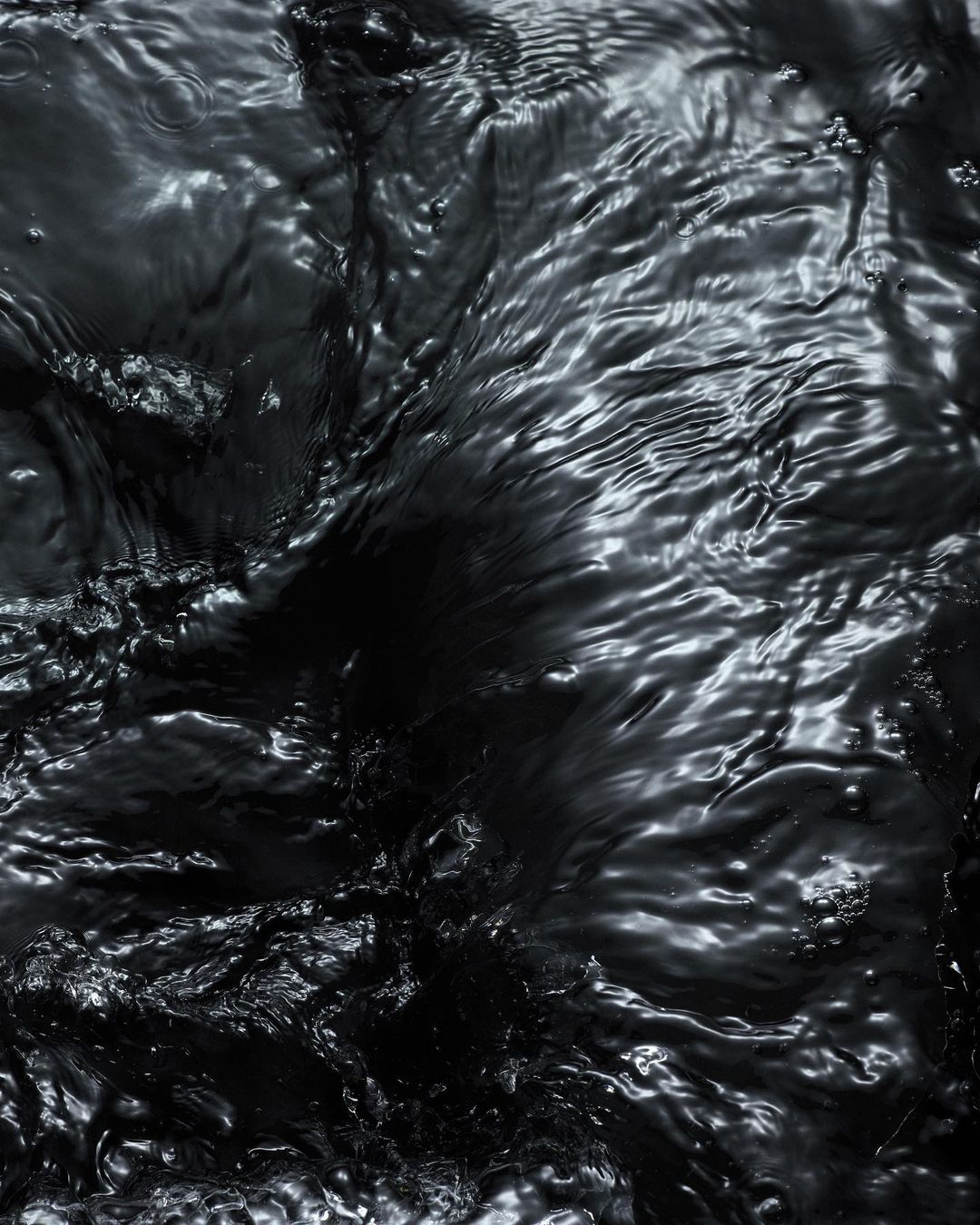 Dark water surface with rippling wave patterns and light reflections creating a textured and dynamic abstract composition.