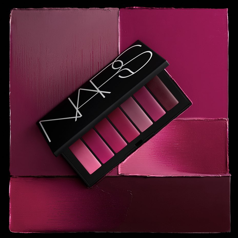 NARS makeup palette sits open with gradient shades of berry against textured berry-toned background squares on black surface.