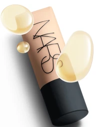 NARS foundation bottle angled against a plain white background with floating liquid droplets by Brenton Carter