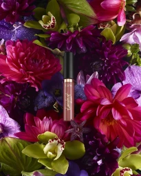 A Tarte cosmetics product tube nestled vertically amidst vibrant purple orchids and magenta dahlias in New York