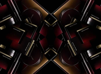 Symmetrical kaleidoscopic arrangement of luxury cosmetics packaging in deep red and black with gold lettering against a dark background.