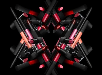 Symmetrical kaleidoscopic arrangement of assorted NARS lipsticks and lip glosses against a solid black background.