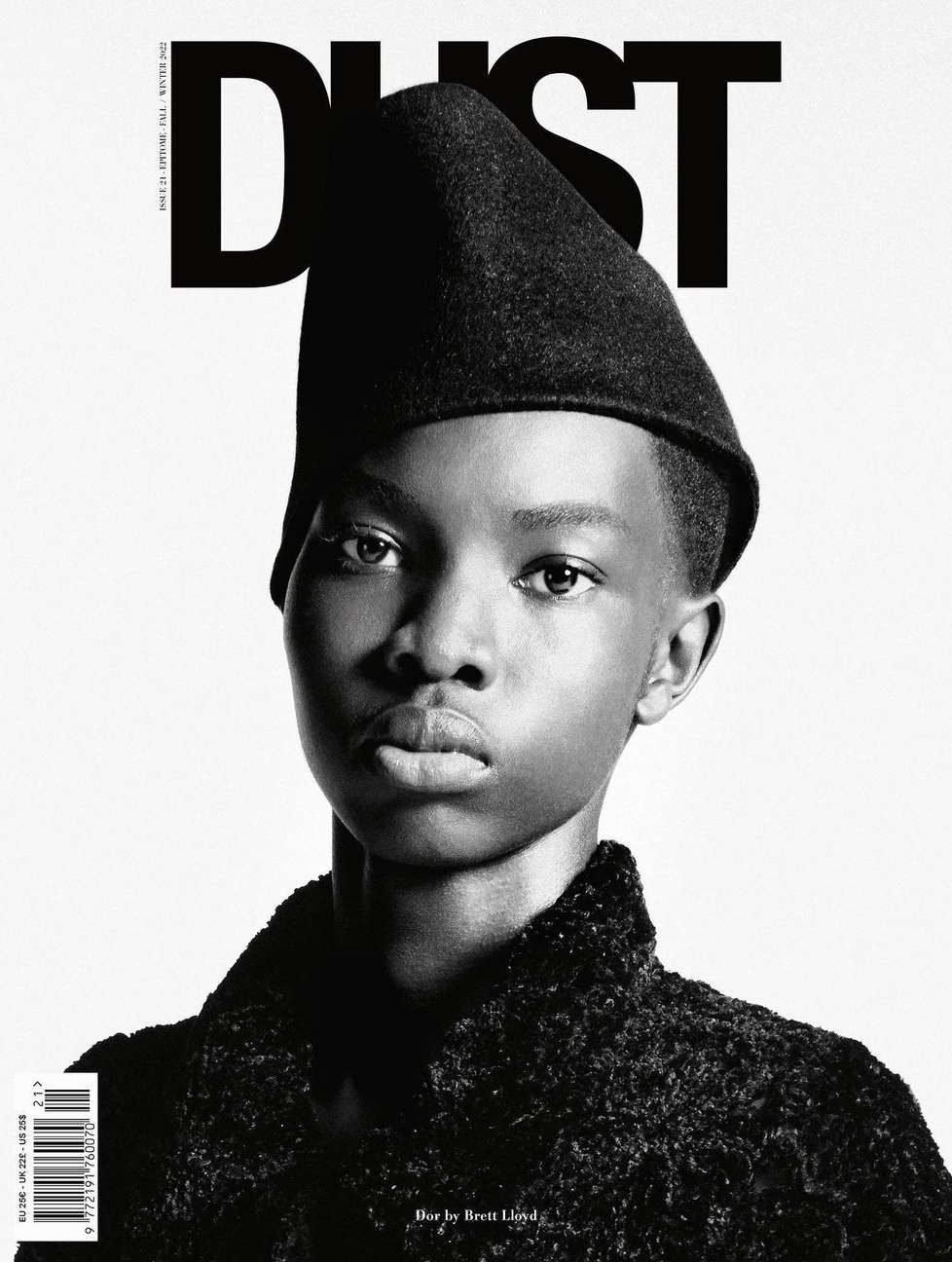 Black and white portrait of African female fashion model wearing a dark colored hat and coat against a plain white studio backdrop.